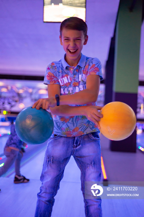 A boy holds bowling balls posing for the camera.