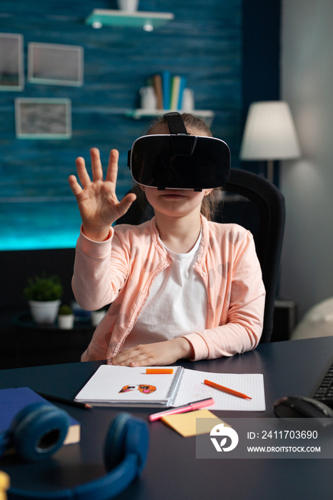 Surprised schollchild looking in VR glasses. experiencing 3D gadget during online lesson sitting at desk in living room. Concept of distance education for kids at home during coronavirus quarantine