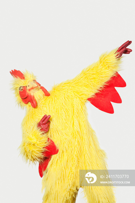 Playful young man in chicken suit against gray background