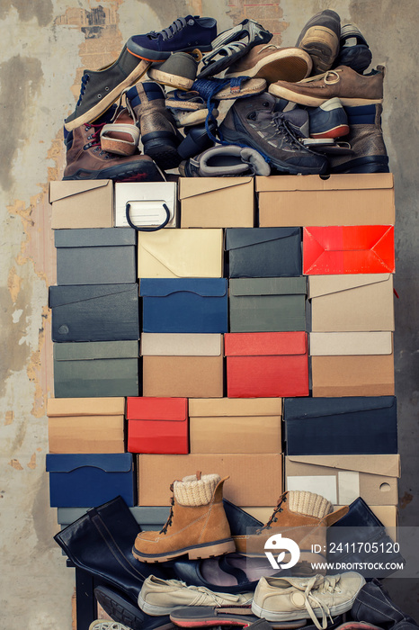 A stack of folded cardboard boxes and a lot of variety of shoes on the background of the shabby wall.