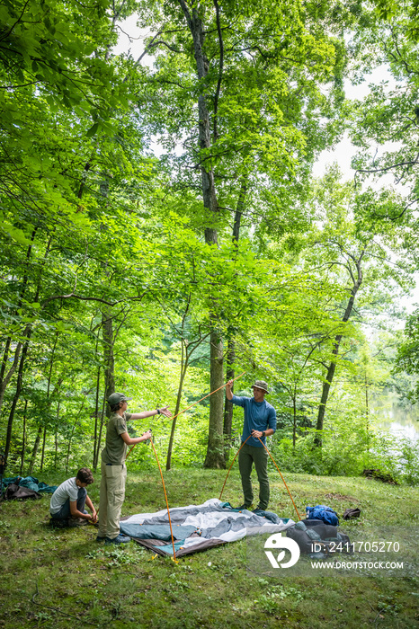 Air Force service member sets up a tent with his sons on  a backpacking trip.