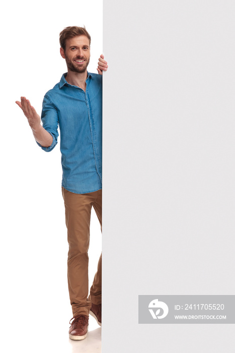 young smiling casual man presenting blank billboard and welcomes