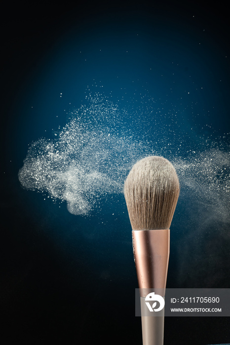 cosmetic brush with stream splash dusty plume of cosmetics on blue background