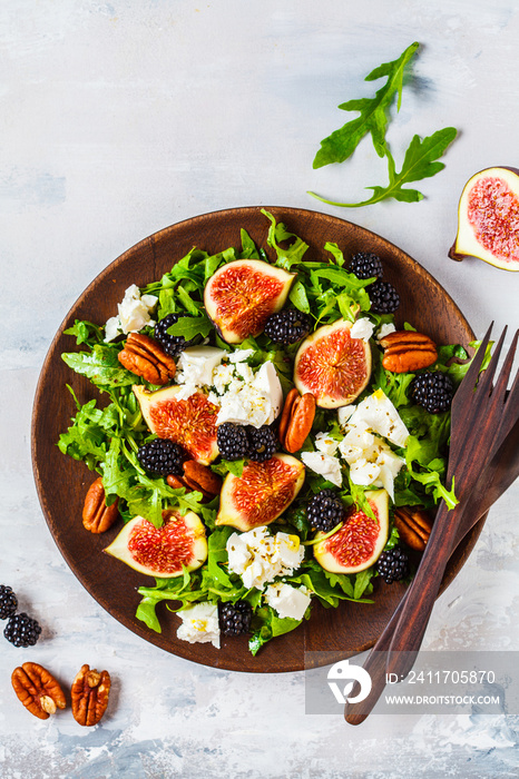 Salad with figs, feta cheese and blackberries in a wooden plate on white background, top view.