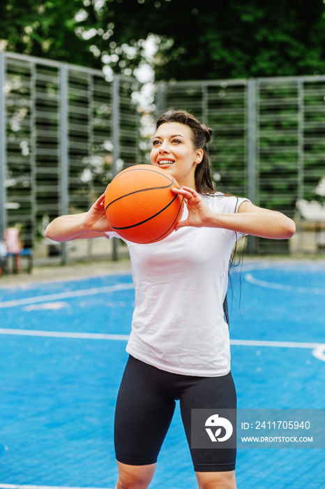 Young athletic woman is training to play basketball on modern outdoor basketball court. Happy woman