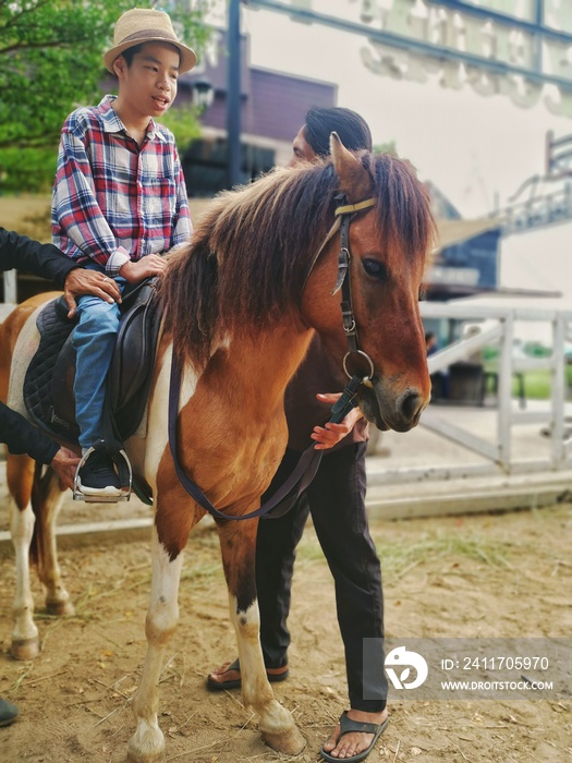 Horse and a child with special needs is riding with a close supervision teacher] This is a treatment called Hippotherapy, Life in the education age of disabled children, Happy disability kid concept.