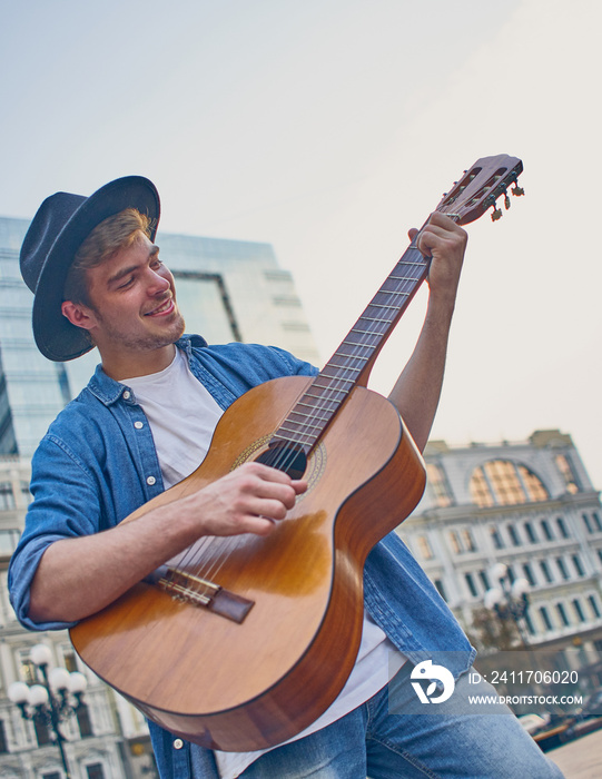 Young man playing the guitar. Stylish hipster guy with hat enjoys music and holidays.