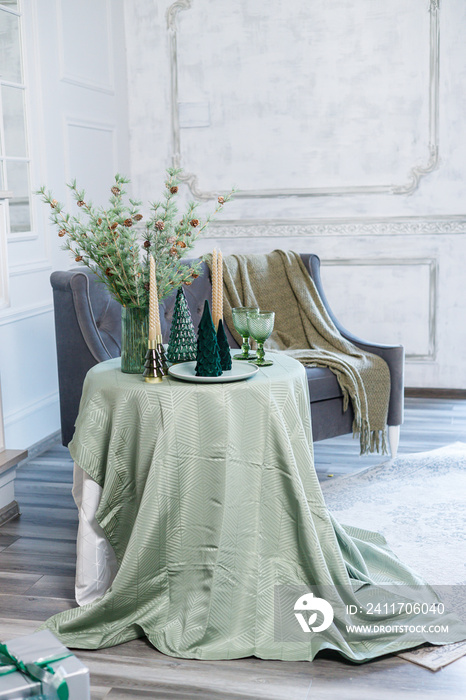 Table setting for Christmas or New Year’s dinner with candles, decorations, tablecloth and napkins on the background of a Christmas tree in an apartment