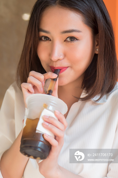 Happy smiling asian woman drinking iced bubble milk tea; aka boba tea, pearl milk tea, tapioca tea, asian exotic beverage concept; retouched image