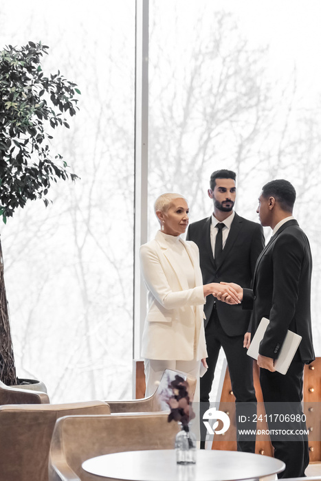 senior businesswoman shaking hands with african american security man near bi-racial bodyguard in hotel.