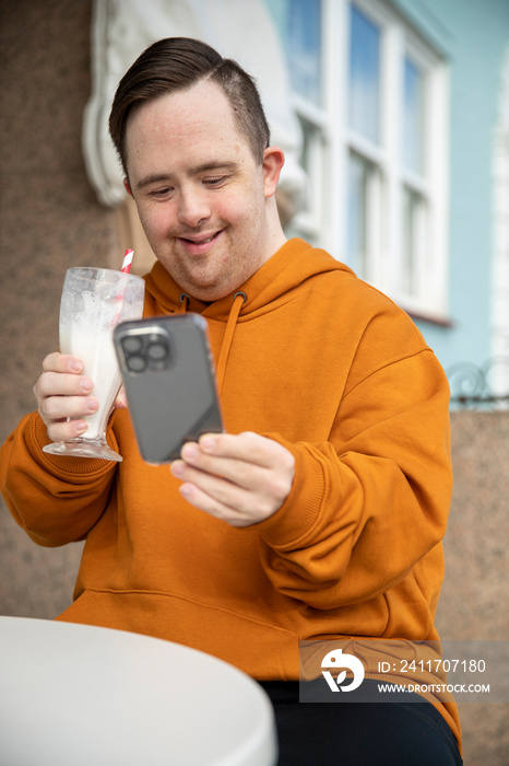 Man in sidewalk cafe drinking milkshake and using phone