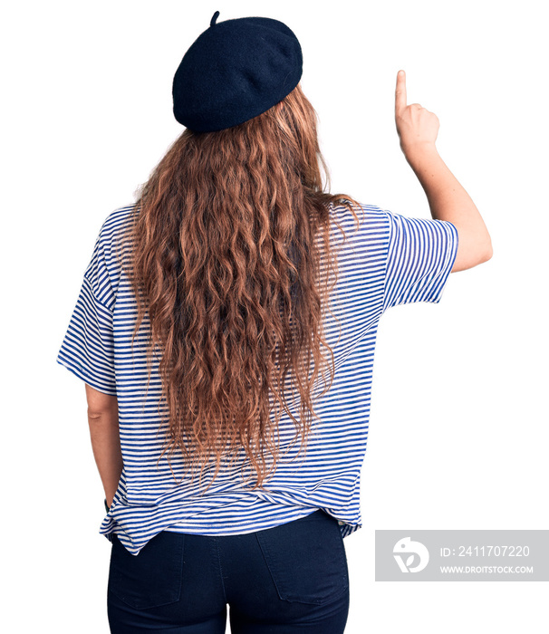 Young beautiful blonde woman wearing french beret and striped t-shirt posing backwards pointing ahead with finger hand