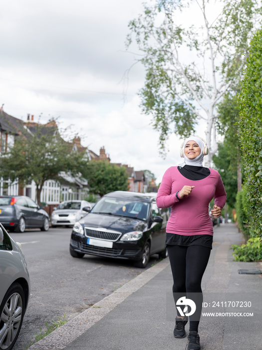 UK,Sutton,Woman in headscarf and headphones jogging on sidewalk