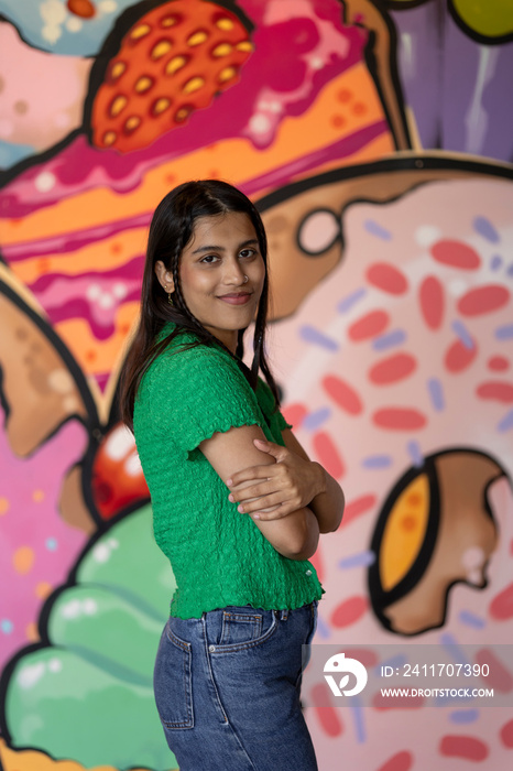 Portrait of smiling young woman standing in front of mural