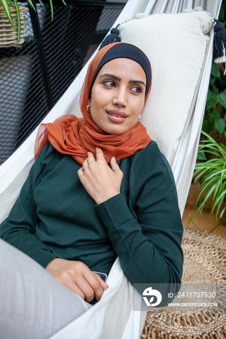 Smiling woman wearing headscarf relaxing in hammock at home