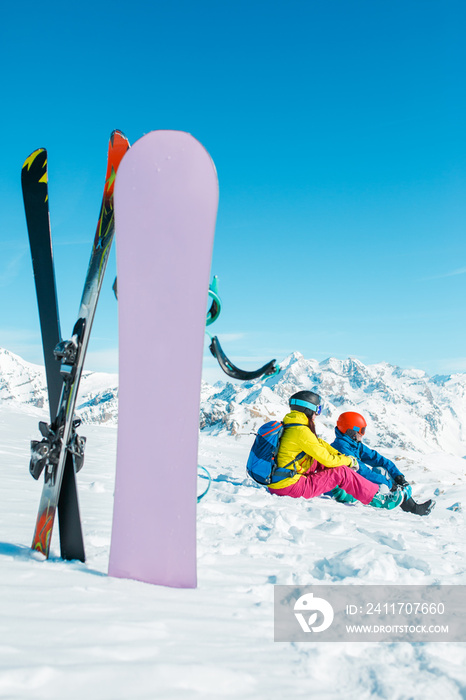Picture of snowboard, skis on background of sitting sports woman and man on snowy hill