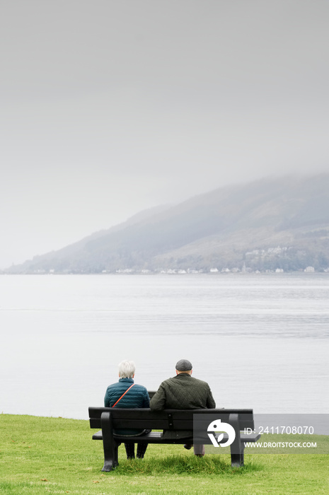 Old senior couple alone on park bench under dark sky