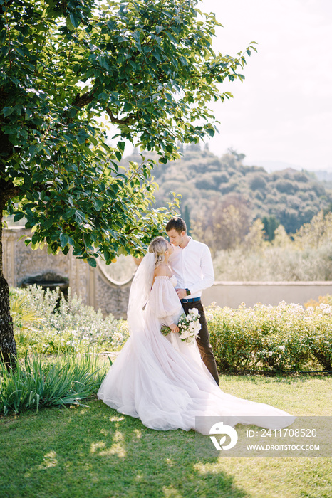 Wedding in Florence, Italy, in an old villa-winery. Bride and groom in the shade of a tree. Wedding couple walks in the garden.