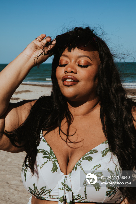 closeup of plus size Black women lifting sunglasses wearing bathing suit top eyes closed