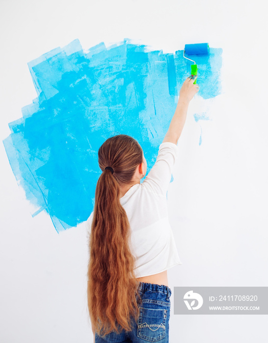 Repair in the apartment. Happy child girl paints the wall with blue paint,