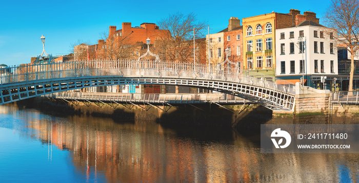 Dublin, panoramic image of Half penny bridge, or Ha’penny bridge, on a bright day with beautiful reflection of historic houses and pubs of the riverside in river Liffey