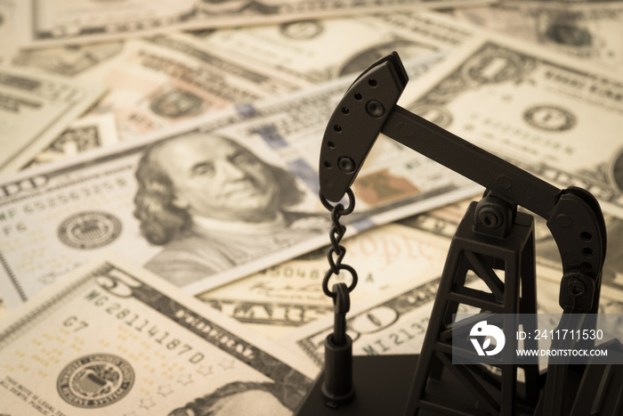 Spending or investment of a country’s revenues from petroleum exports industry (Petrodollar). Oil pump jack on US dollar banknotes. Concept of crude oil production, petroleum industry or petrodollar.