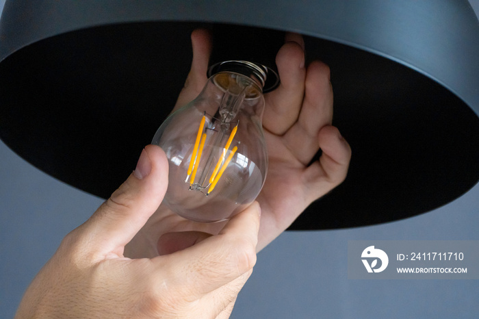 Close-up. A hand changes a light bulb in a stylish loft lamp. Spiral filament lamp. Modern interior decor.