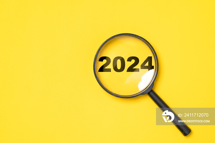 2024 year inside of magnifier glass on yellow background for focus and preparation new year change and start new business target strategy concept.