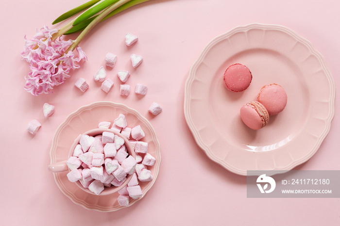 Pink marshmallow and pink macaroons in pink dishes and pink hyacinth on pink background