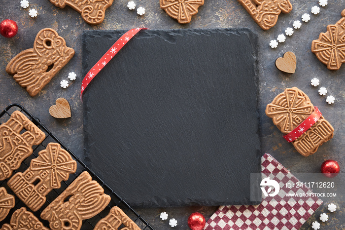 Speculoos or Spekulatius, Christmas biscuits, chocolate balls and stripy towel on dark textured background. Traditional German sweets, cookies for Xmas, Advent. Copy-space on black slate stone plate.