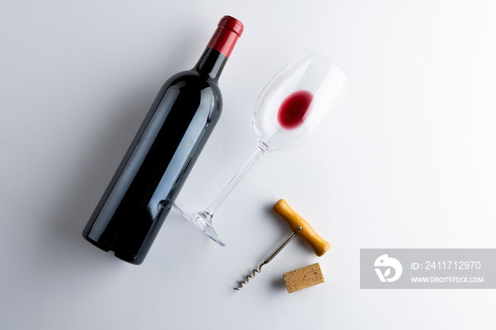 Bottle of red wine, glass and corkscrew on white background, with copy space