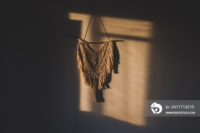 Macrame wall hanging in the sunny spot of the room. DIY boho wall tapestry hanging on the wall in the morning sun