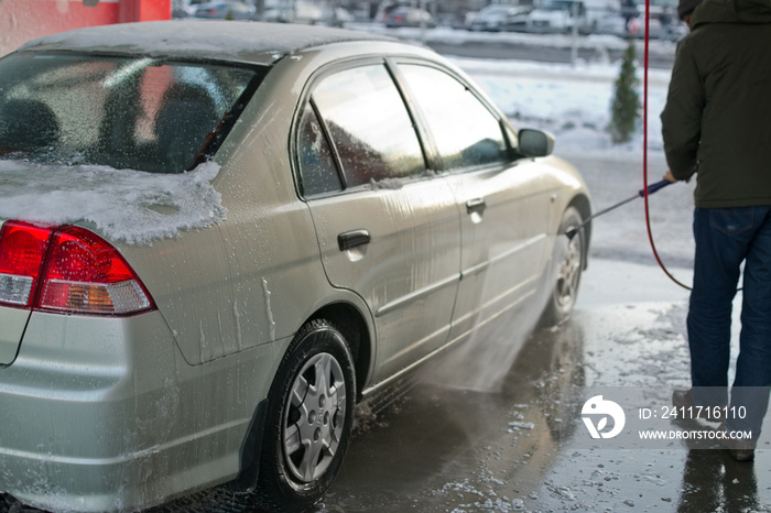 Man is washing his automobile at manual car wash station at winter