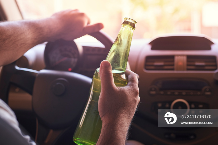 An unrecognizable man drinking beer while driving car. Concepts of driving under the influence, drunk driving or impaired driving