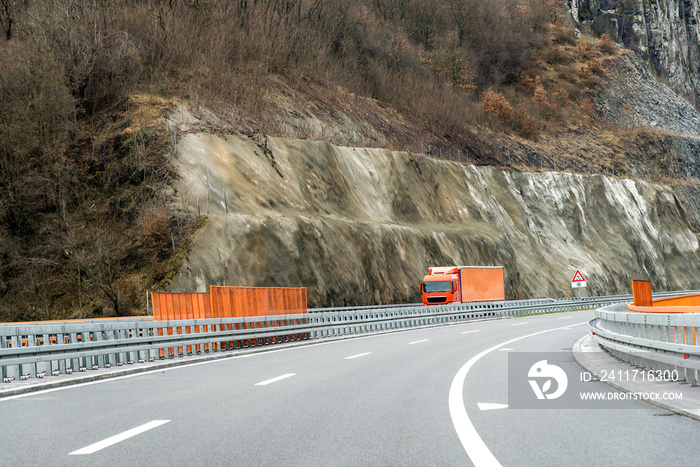 Orange truck driving on asphalt road in a rural landscape.