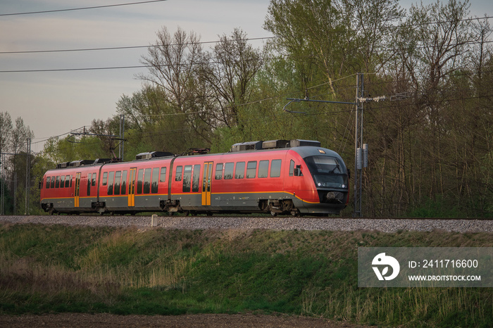 Red modern commuter passenger train in a rural environment. Slovenian german made passenger train on a cloudy day.