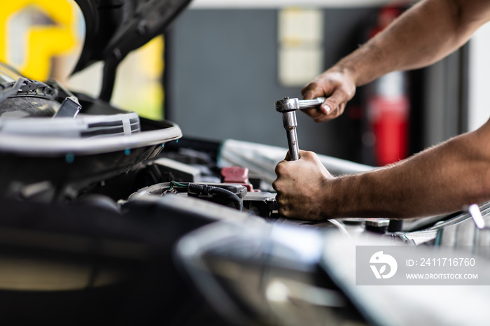 Caucasian male mechanic repairs car in garage. Car maintenance and auto service garage concept. Closeup hand and spanner.