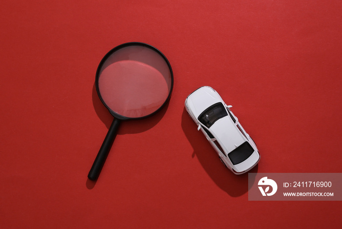 Toy car model and magnifying glass on red background