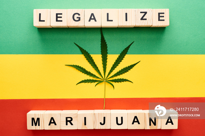 top view of cannabis leaf and wooden blocks with legalize marijuana lettering on Rastafarian flag background