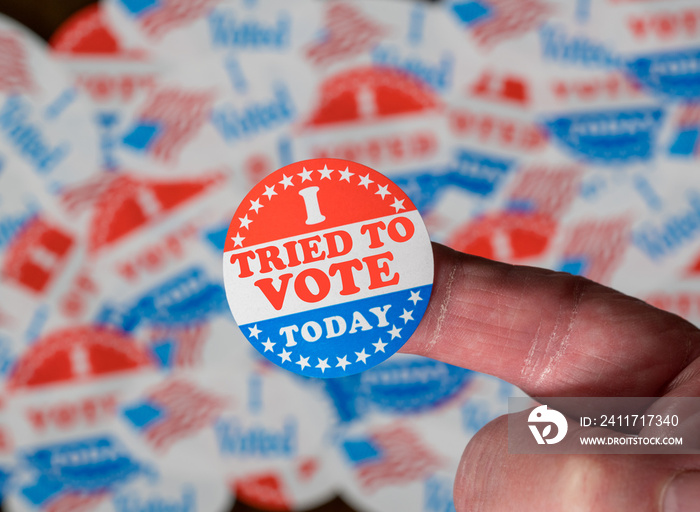 Finger with I Voted button in front of voting stickers given to US voters in Presidential election to illustrate vote suppression or rejections