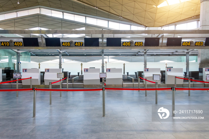 Empty check-in desks for drop off baggage with paths canceled with a red ribbon to differentiate passengers at the airport terminal.