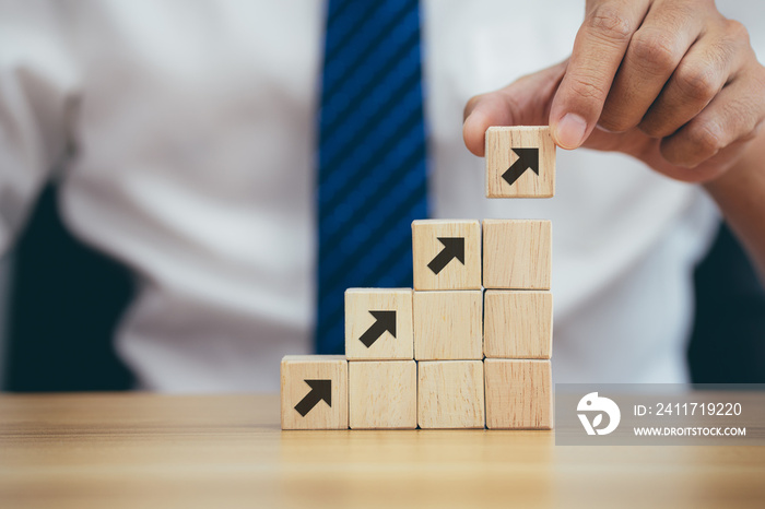 Closeup man hand arranging wood cube stacking as step stair to goal with arrow up symbol, business concept growth success process.