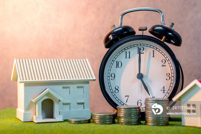 Real estate investment or Home mortgage loan rate. Property ladder concept. Coins stack, house model and table clock on green grass. Investment and business growth background