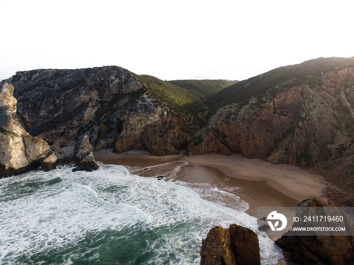 Aerial panorama of waves crashing on shore of Praia da Ursa atlantic coast rocky cliff sand beach Sintra Lisbon Portugal