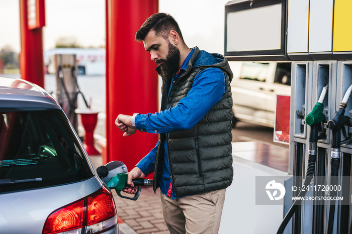 Young handsome adult man standing on gas station and fueling his car.