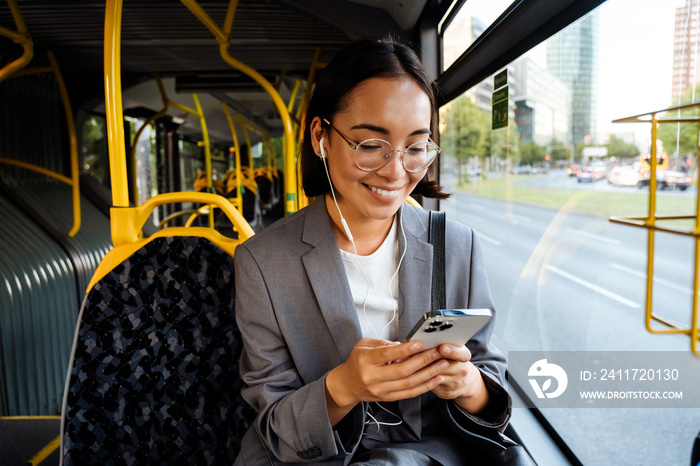 Woman wearing earphones and looking at phone screen while traveling in bus