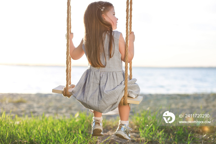 Cute little girl playing on swing near river