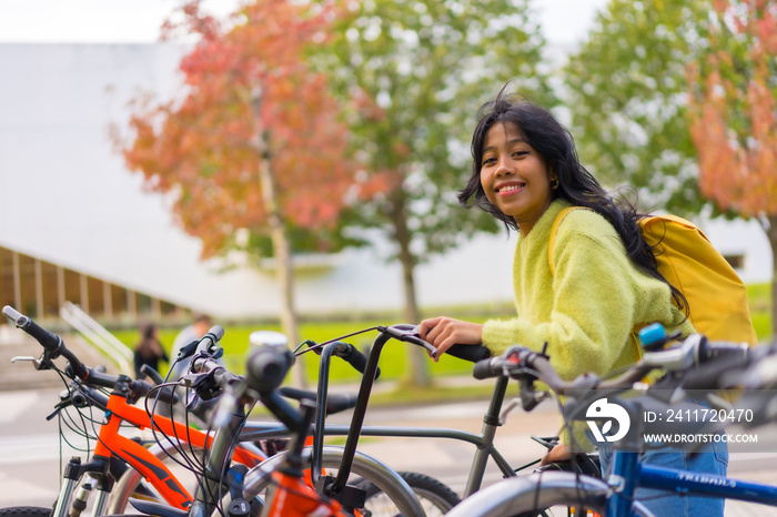 Portrait of smiling Asian female student parking bicycle at college campus