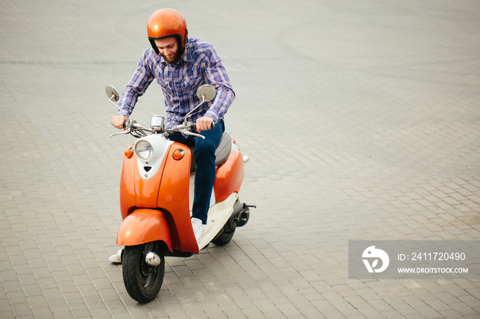 Hipster young  man in helmet is riding on yellow retro scooter in town