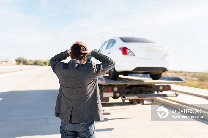 Angry man seen from behind watching his car being towed